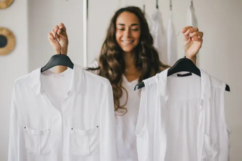 Woman holding two white tops on hangers in front of her.
