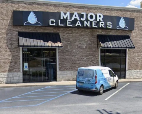 A van parked in front of a brick building with a sign that reads "Major Cleaners." The van and building both display the business logo.