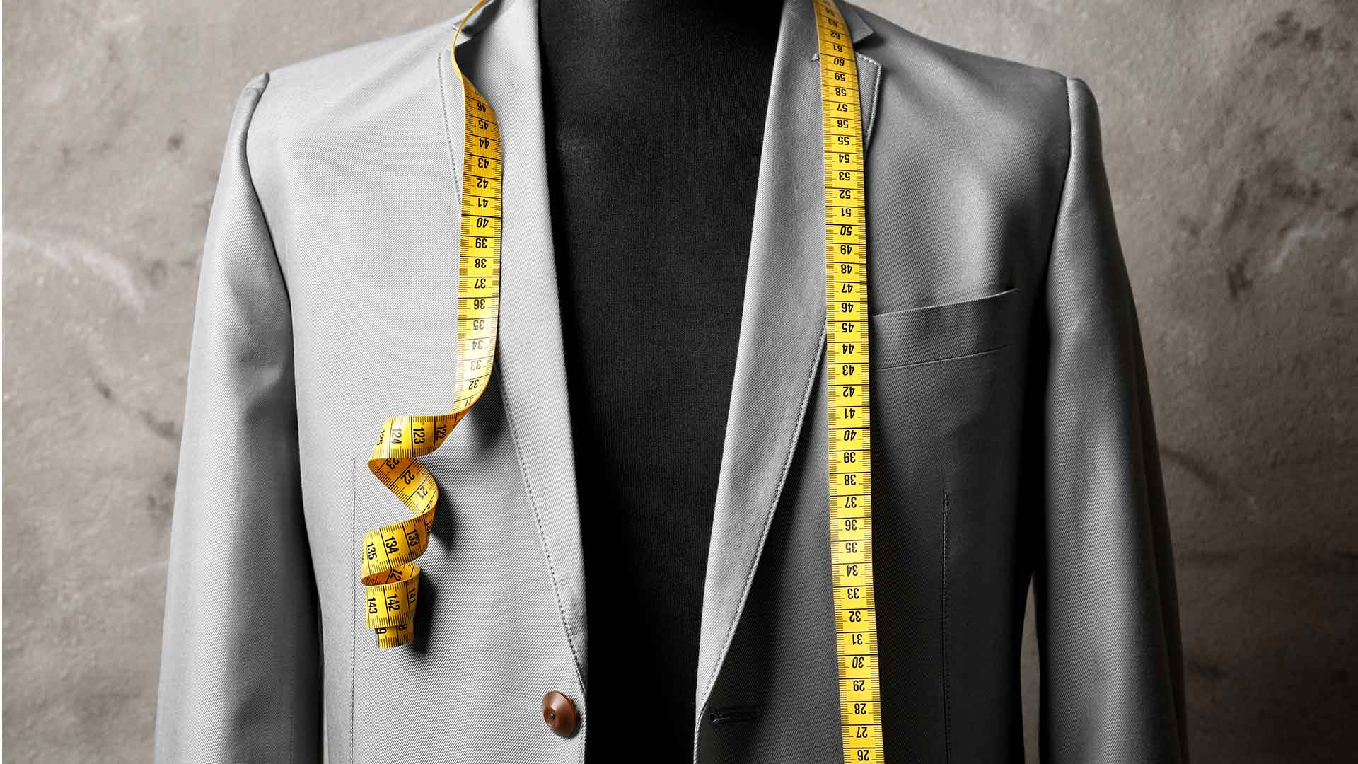 A mannequin wearing a grey suit with a measuring tape.