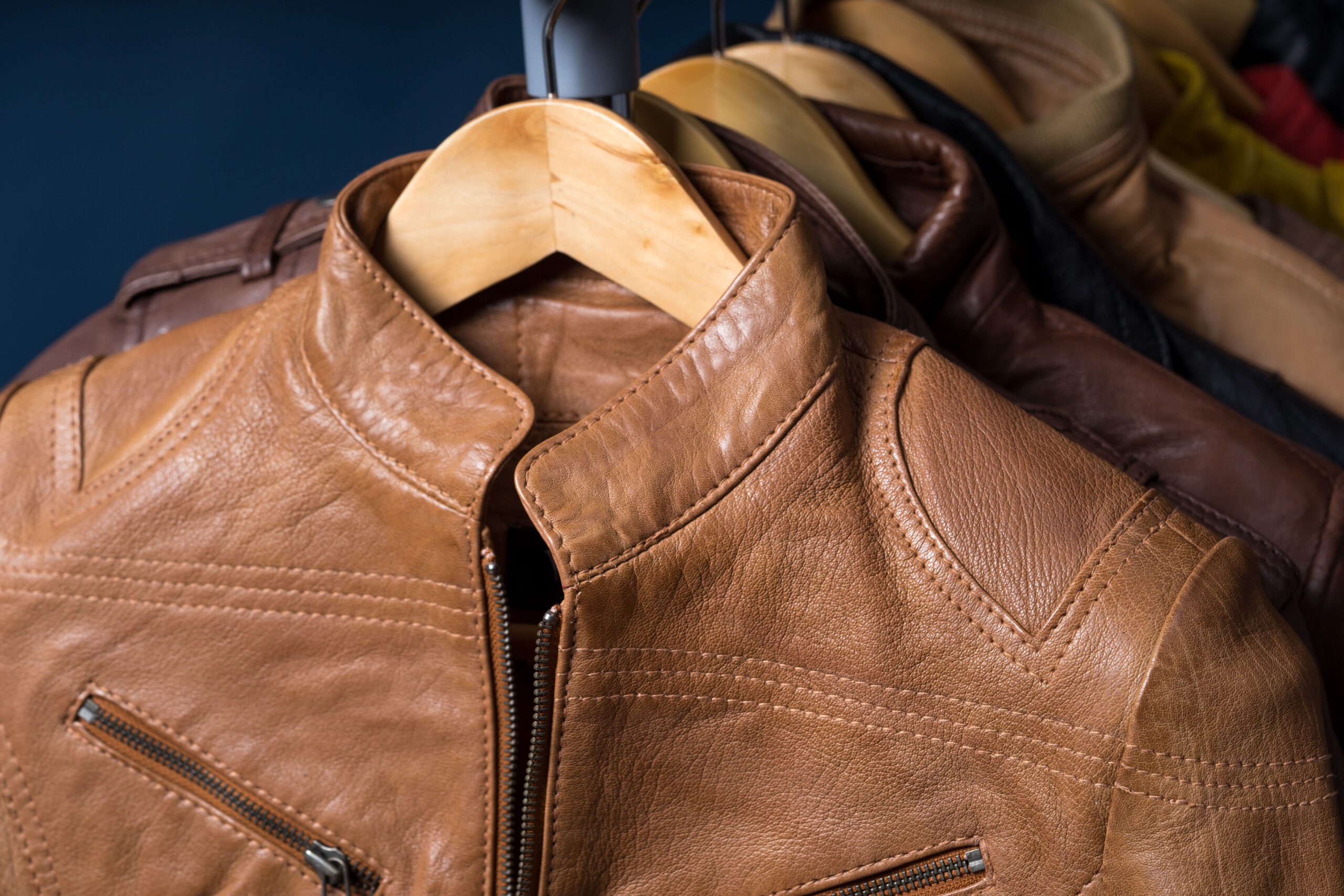 Different color leather jacket hanging on rack on blue background