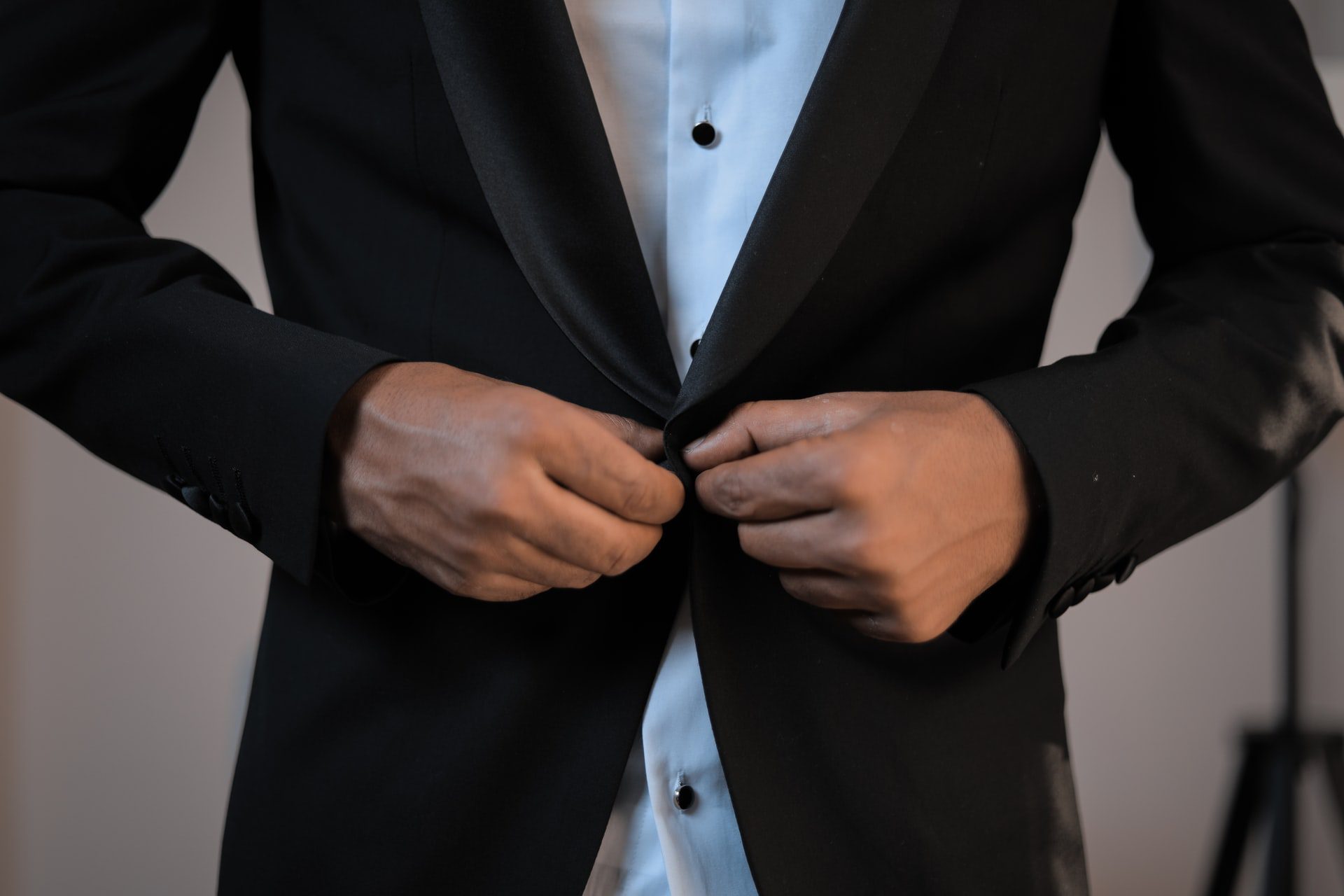 A person buttoning a black suit jacket over a white shirt.