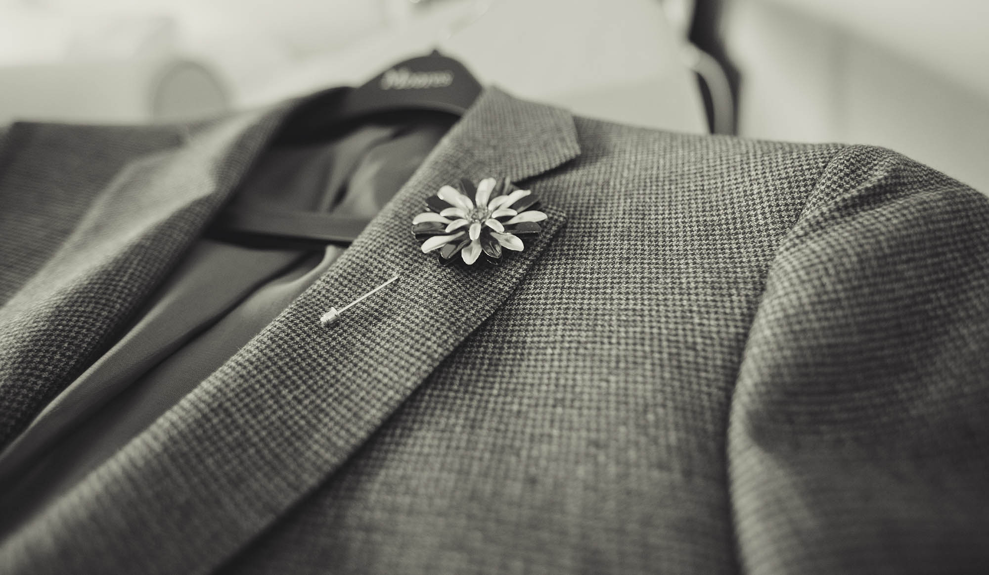 Close-up of a gray suit jacket with a floral lapel pin and a shirt underneath.