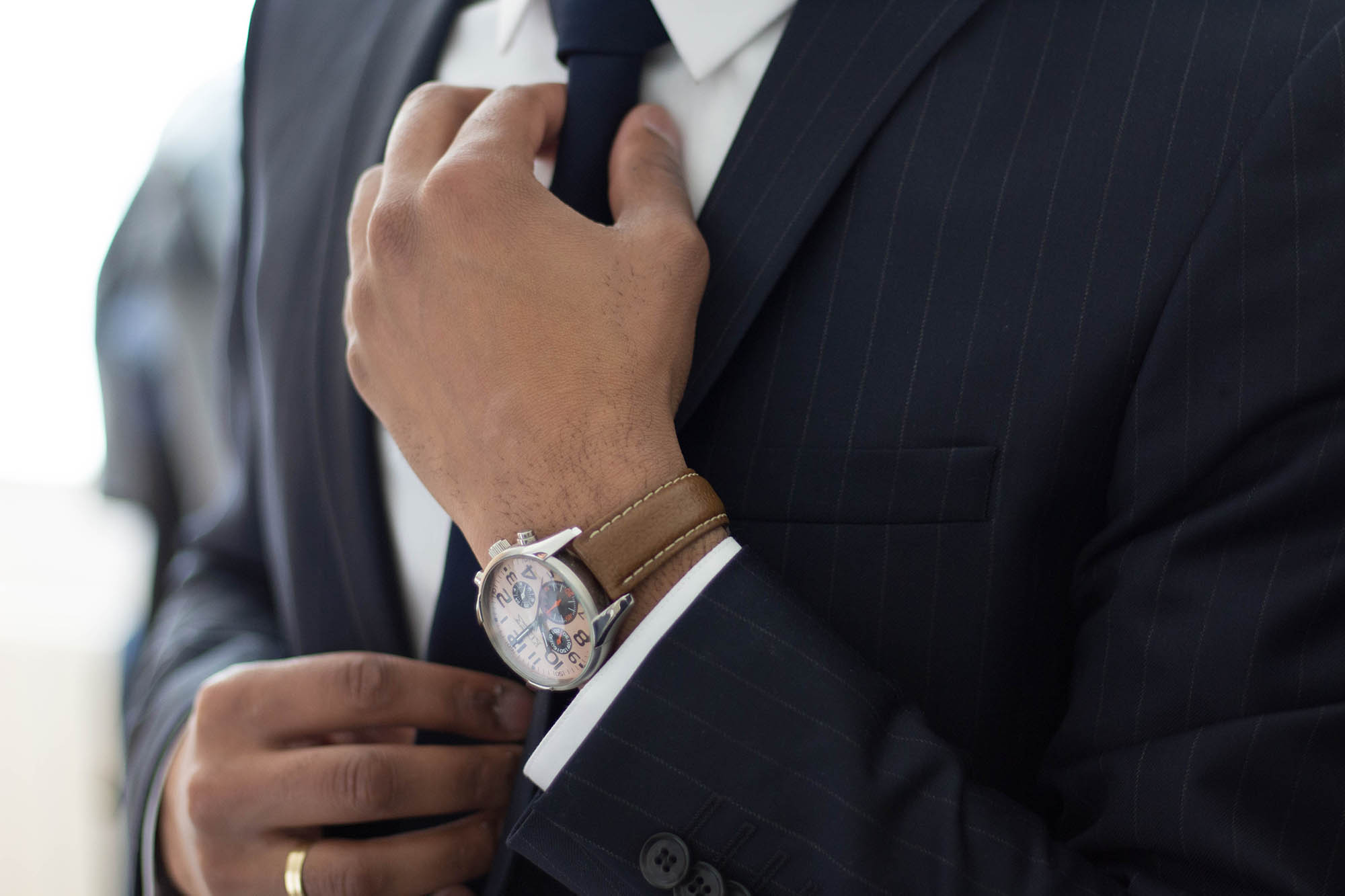 Person adjusting a navy pinstripe suit and tie, wearing a watch with a brown leather strap.