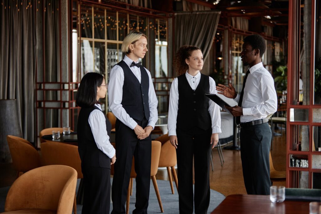 Four people in restaurant attire have a discussion inside a dining area with curtains and soft lighting.