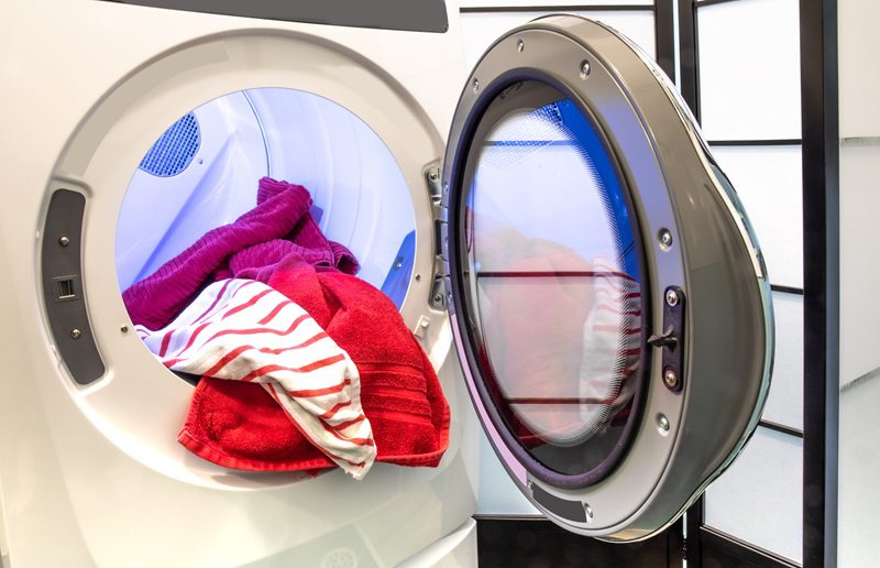Front-loading washing machine with its door open, showing red and striped towels inside the drum.